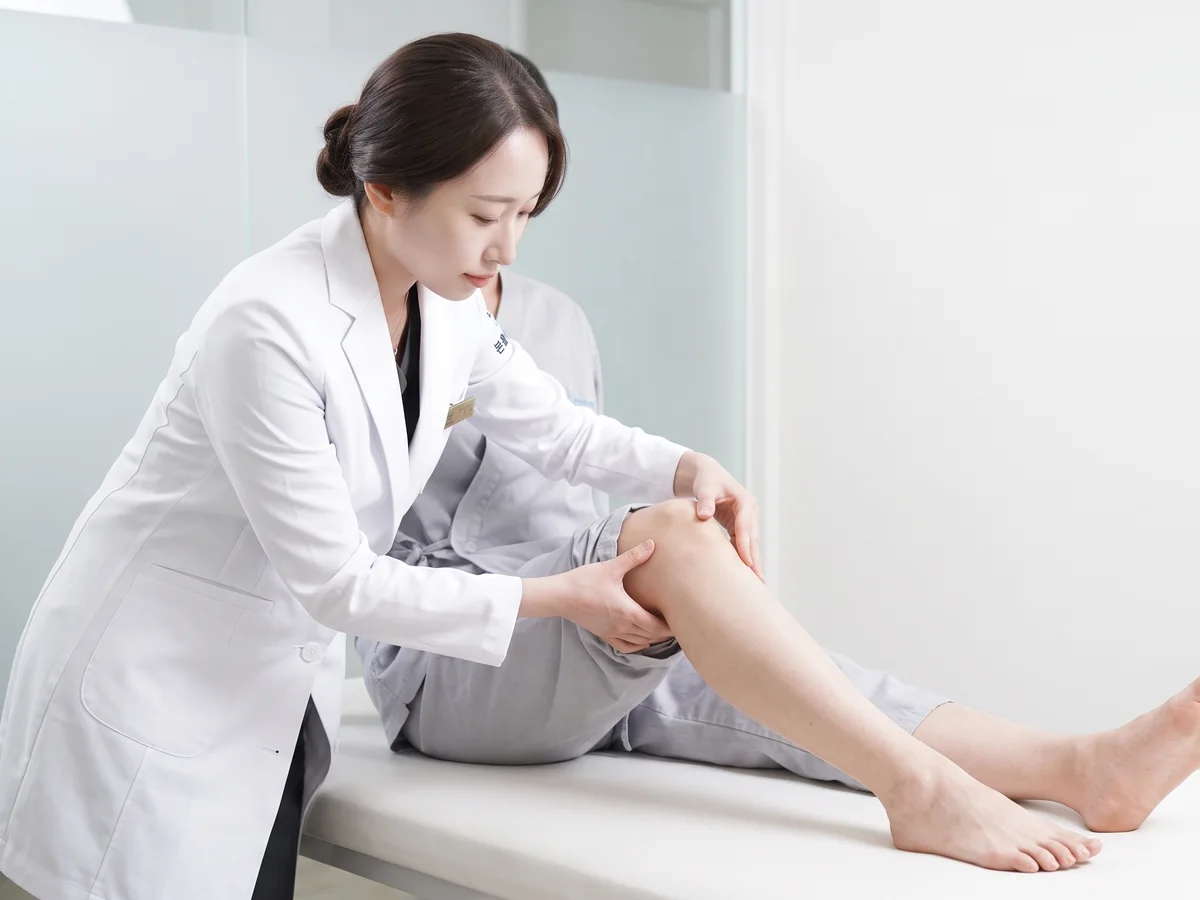 침대에 앉은 환자의 무릎을 굽혀 상태를 살피는 한의사
